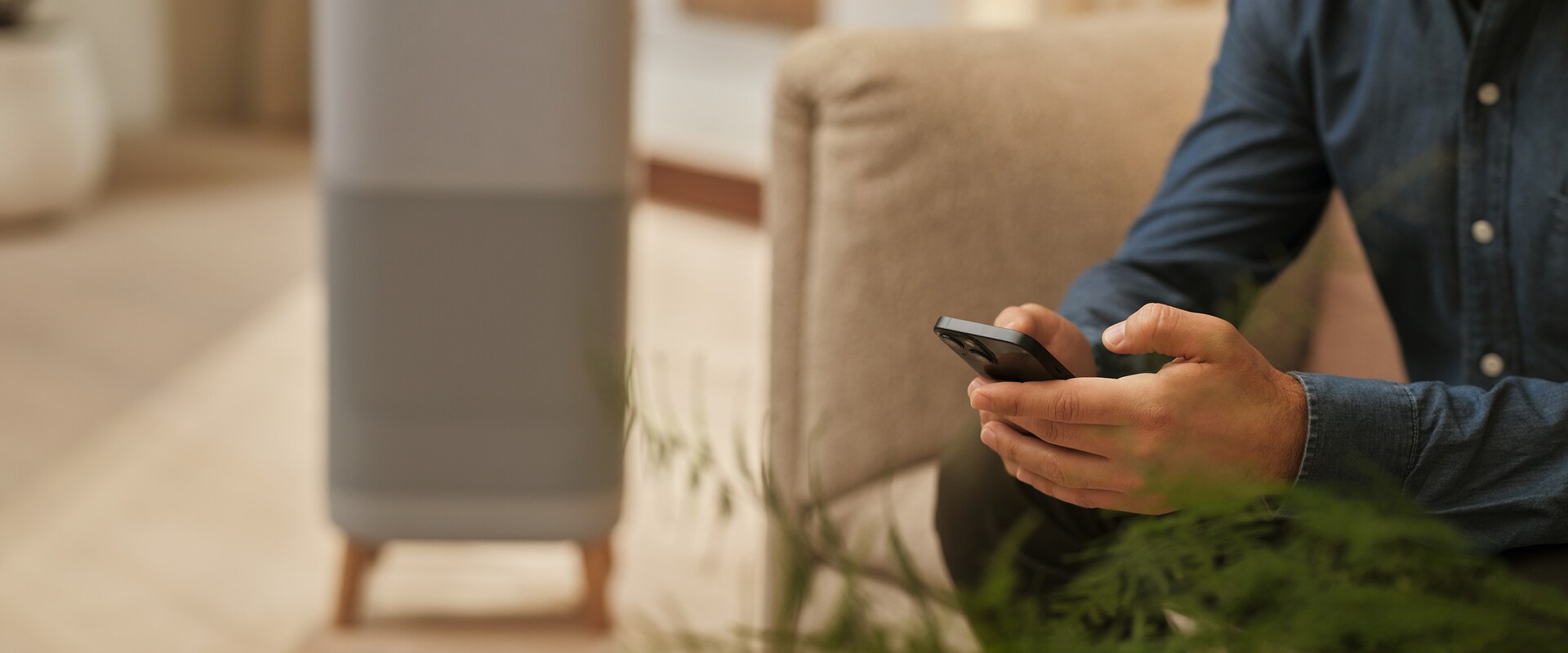 Muž s mobilom na pohovke, blízko čističa vzduchu.